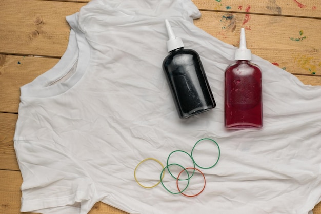 Un T-shirt blanc à colorier et des bouteilles de peinture sur un fond en bois Mise à plat