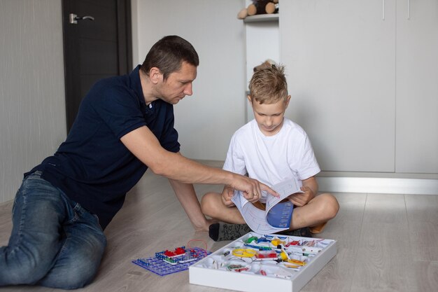 T-shirt blanc concepteur électrique beaucoup de détails garçon et homme père et fils s'asseoir sur le sol jouer à un jeu lire les instructions personne