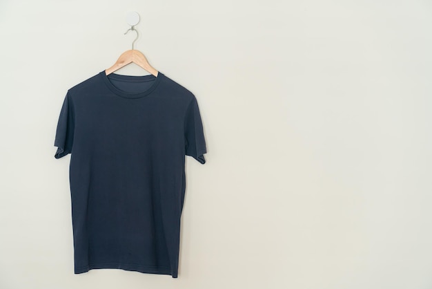 t-shirt bleu marine suspendu avec un cintre en bois au mur