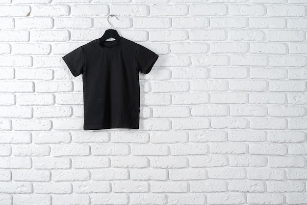 T-shirt noir accroché sur un cintre contre le mur de briques