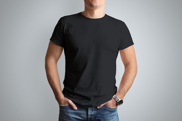 T-shirt noir devant sur un jeune homme musclé isolé sur un mur gris.