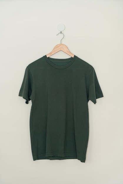 t-shirt vert foncé suspendu avec un cintre en bois au mur