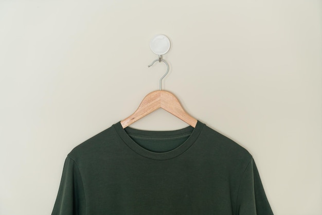 t-shirt vert foncé suspendu avec un cintre en bois au mur