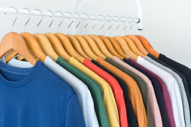 T-shirts colorés sur un cintre en bois suspendu à un porte-vêtements sur fond blanc