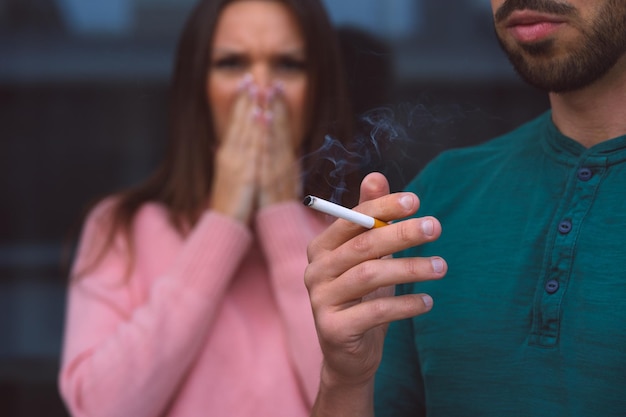 Tabagisme passif Homme fumant une cigarette près d'une femme couvrant son visage de la fumée de cigarette