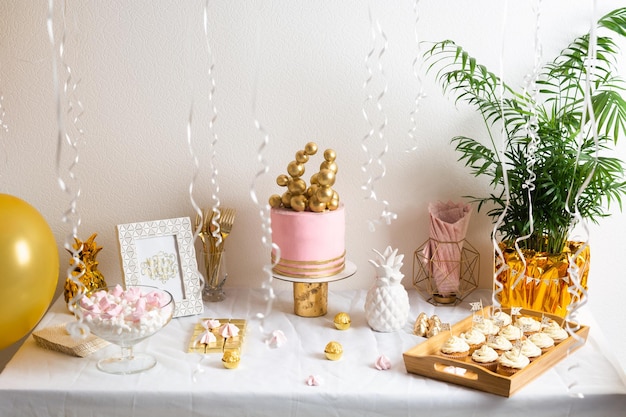 Table d'anniversaire de vacances avec gâteau et ballons décoration rose et dorée