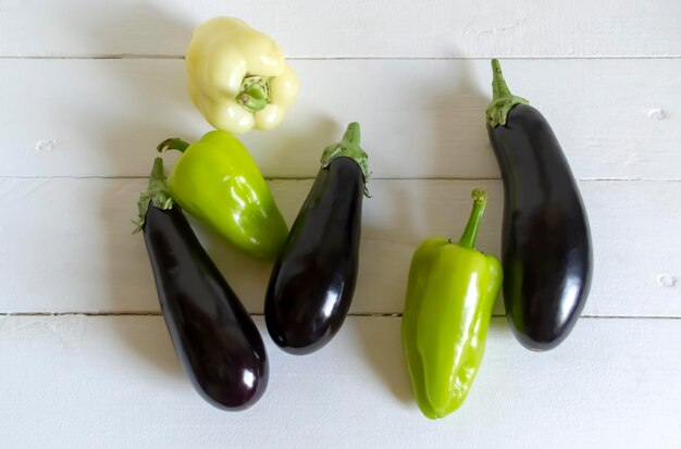 Sur une table blanche, des aubergines et des poivrons. Des poivrons et des auburgines sur la table. Des légumes d'été à la table.