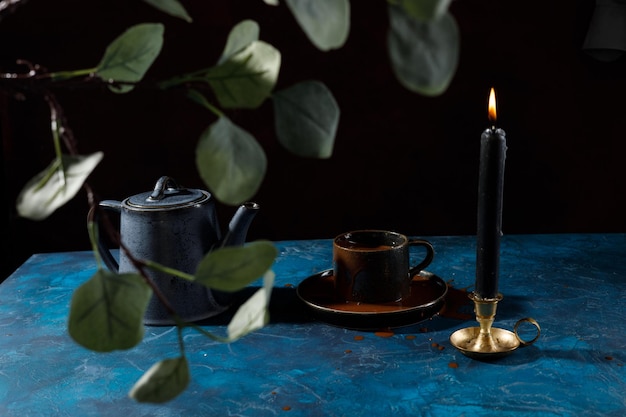 sur la table bleue il y a une bougie noire, une tasse de café et une théière bleue