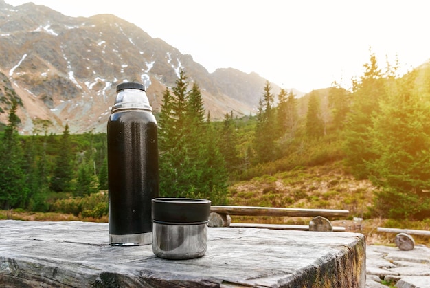 Photo table en bois avec des bancs sur une plate-forme en pierre parmi les montagnes thermos avec boisson chaude