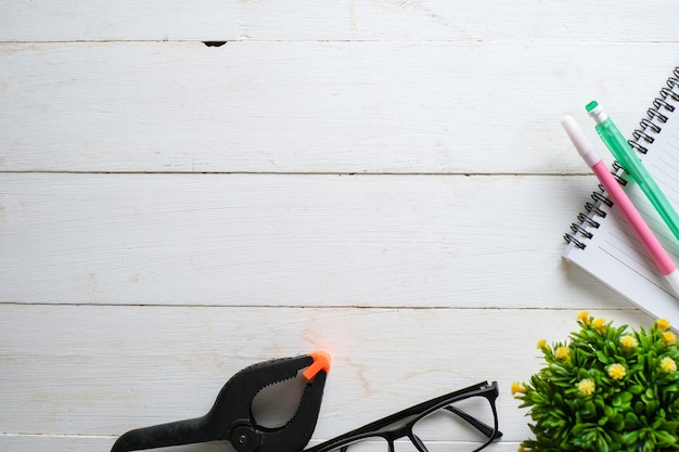 Table en bois blanc avec carnet de notes, lunettes, stylo, plantes décoratives. Vue de dessus avec espace de copie, mise à plat.