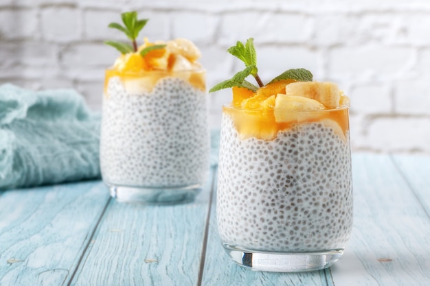 Sur une table en bois bleu, pudding de chia à la banane dans deux verres en verre avec des graines de chia crues