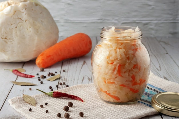 Sur une table en bois, choucroute aux carottes et épices dans un bocal.