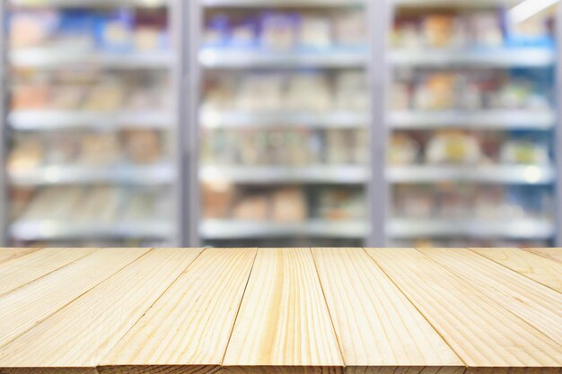 Table en bois avec congélateur de réfrigérateurs commerciaux de supermarché montrant des aliments surgelés arrière-plan flou