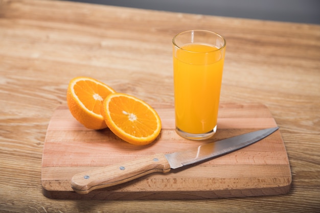 Sur une table en bois un couteau, un verre avec une boisson et une orange