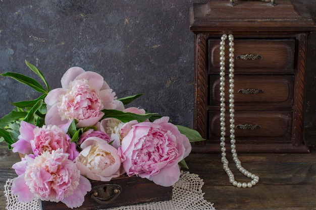 Sur une table en bois dans une boîte décorative des pivoines et une vieille boîte avec des perles de perles