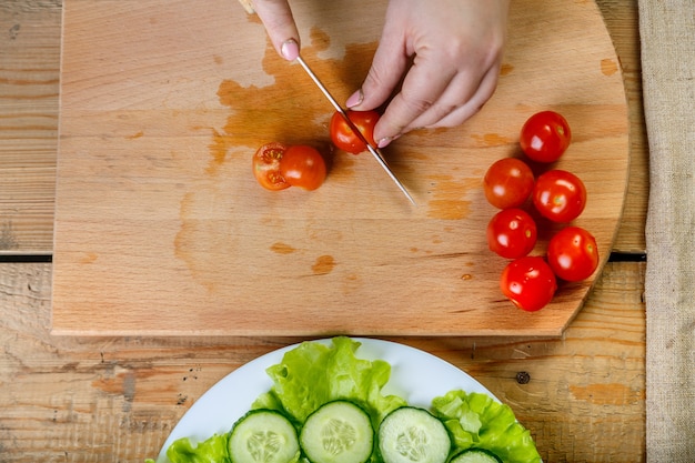 Sur une table en bois, une femme prépare un régime de tomates pour une salade de légumes. Vue de dessus