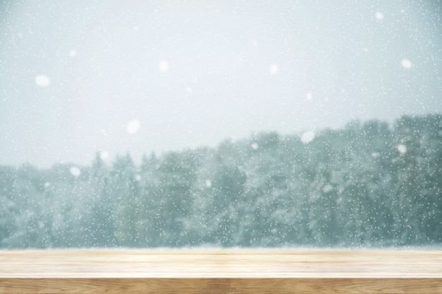 Table en bois avec forêt couverte de chutes de neige en hiver. Tonalité de couleur vintage et style rustique.