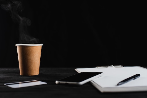 Sur la table en bois noir téléphone carte de crédit feuille de papier blanche dans le dossier souris et stylo et tasse à café jetable