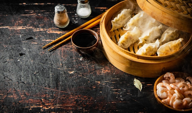 Photo une table en bois avec un panier à vapeur en bambou rempli de boulettes et un récipient en bois de sauce soja.