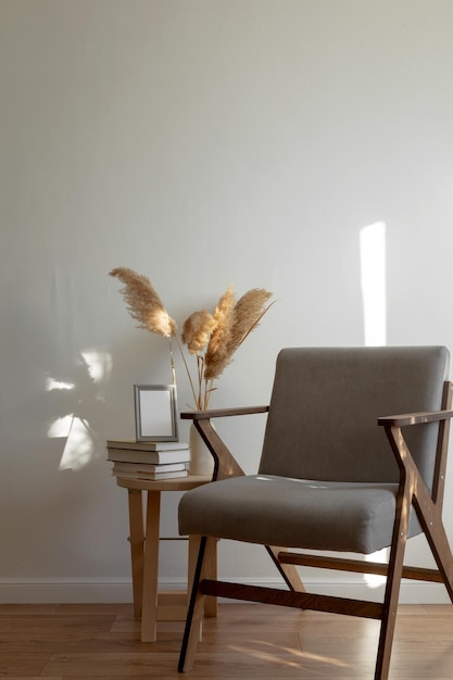 Table en bois avec pile de livres et vase avec maquette d'herbe de pampa cadre gris chaise grise Intérieur scandinave minimaliste clair