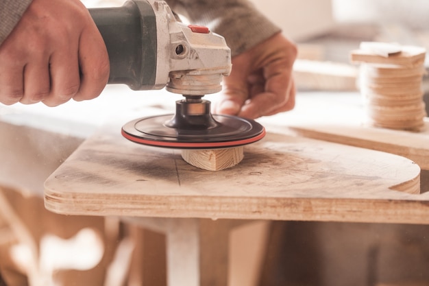 Table en bois de polissage de travailleur où les mains de charpentier poncent un bois avec une ponceuse électrique