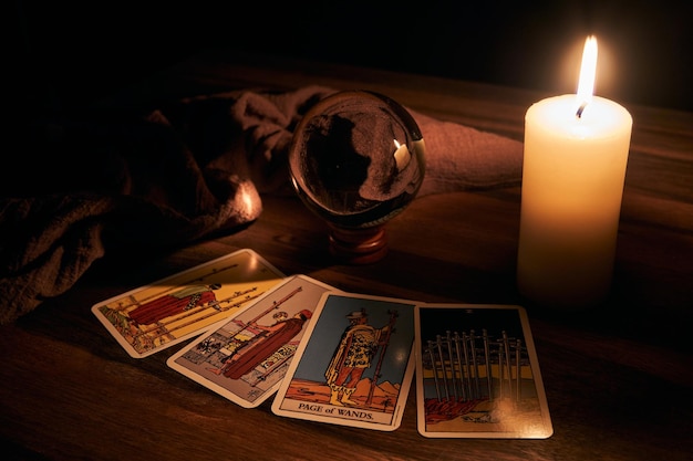 table en bois révélatrice de bonne aventure et bougie blanche avec une boule de cristal et un fond de cartes de tarot