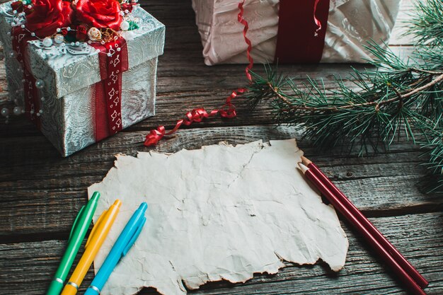 Sur la table en bois se trouvent un vieux papier jaune, rouge, crayons, stylos couleurs assorties cadeau et branches d'arbres pour la nouvelle année