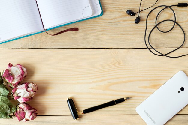 table en bois avec smartphone, casque, stylet, agenda et roses et feuilles séchées