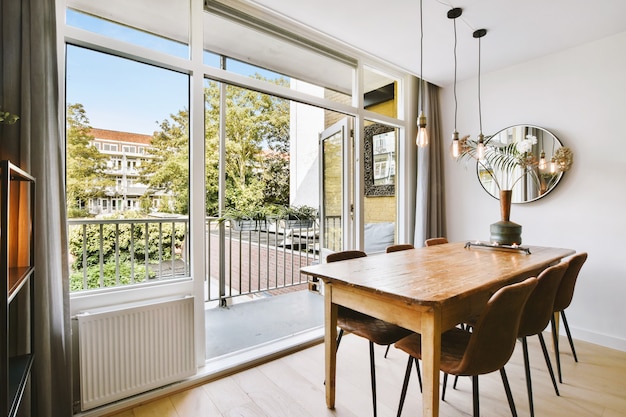 Table en bois avec vase et chaises placés près de la porte du balcon ouverte dans la salle à manger lumineuse à la maison