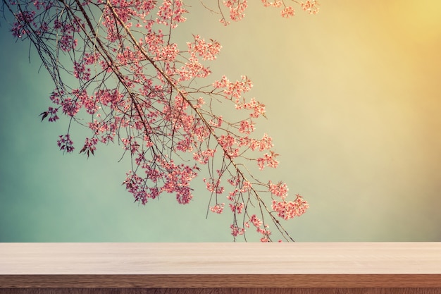 Table en bois vide pour le placement de produits ou le montage et la floraison rose avec des tons vintage.