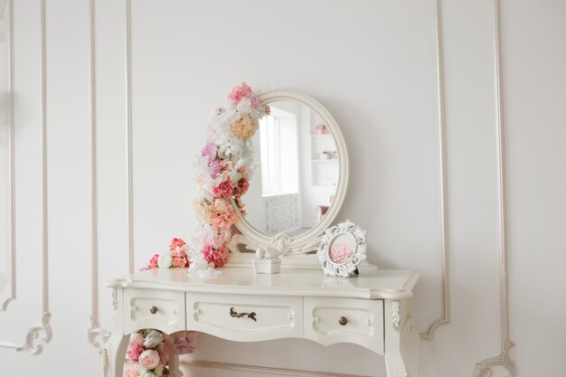 Table boudoir de style vintage avec miroir rond et fleurs. Chambre lumineuse blanche.