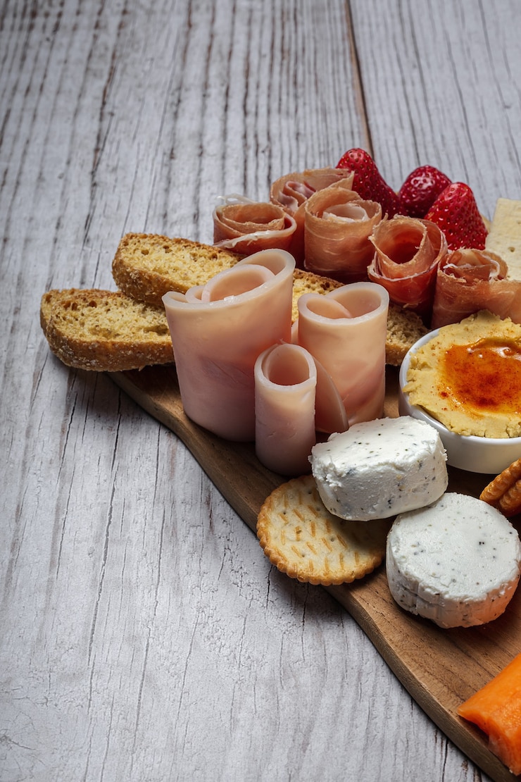 Photo table de brunch santé à emporter avec jambon, fraises; kiwi; pain; biscuits; fromage, carottes, mandarines, houmous.