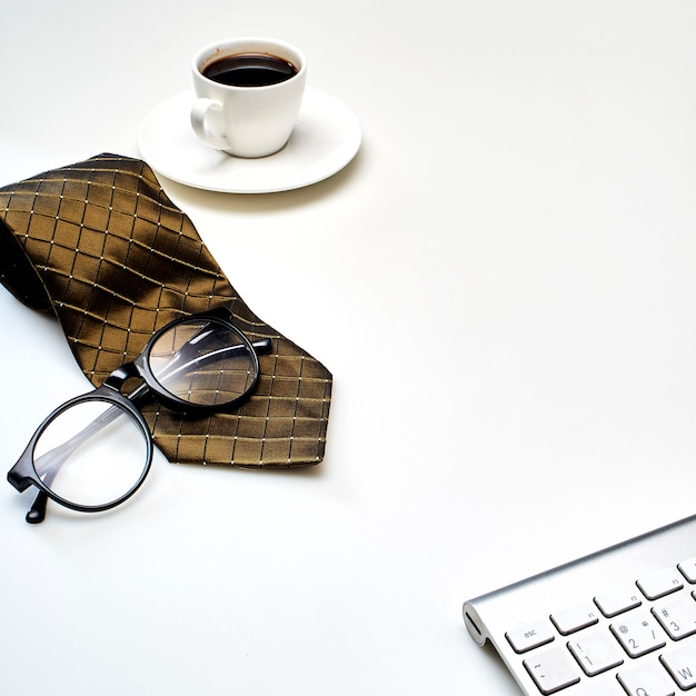 Table de bureau blanche moderne avec une tasse de café, une cravate et d’autres fournitures.