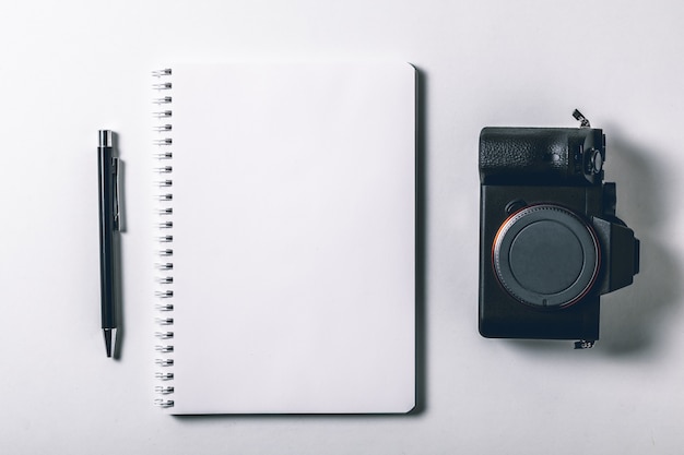 Table De Bureau Blanche Avec Stylo Et Appareil Photo Numérique Sans Miroir. Page De Cahier Vierge