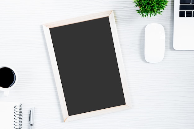 Table de bureau en bois blanc et équipement pour travailler avec du café noir et un tableau blanc dans la vue de dessus et ray plat