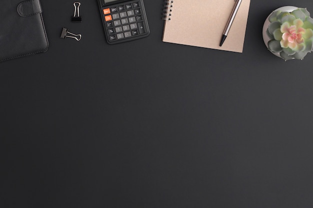 Table de bureau en cuir noir avec calculatrice, cahier et plante verte. Vue de dessus avec espace de copie