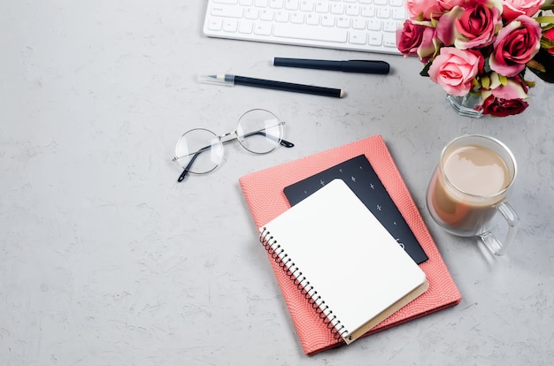 Table de bureau grise avec cahiers, blanc vide, fournitures, verres et tasse de café. Vue de dessus avec un espace pour votre texte. Mise à plat. Bureau à domicile de style minimal ou espace de travail indépendant moderne.