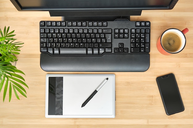 Table de bureau d'en haut avec clavier noir tablette graphique smartphone tasse de café et une plante aux feuilles vertes