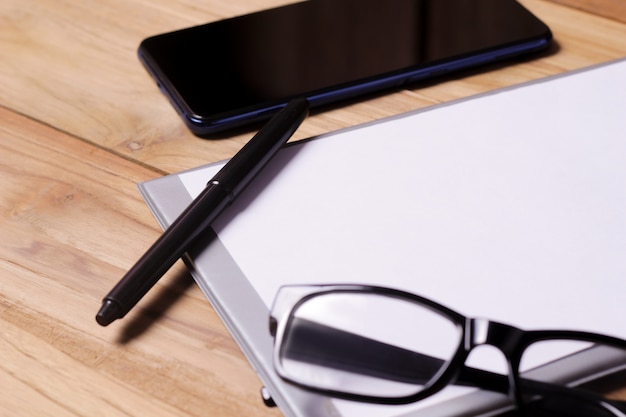 Table de bureau avec des lunettes, un stylo à note courte et un smartphone.