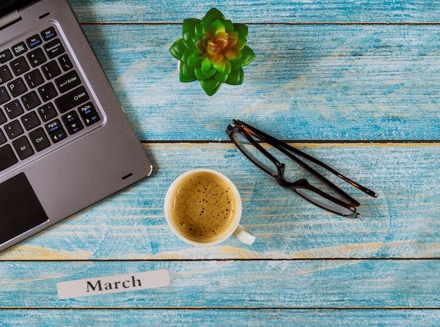 Table de bureau avec mois de mars de l'année civile, ordinateur et tasse à café, vue sur les verres