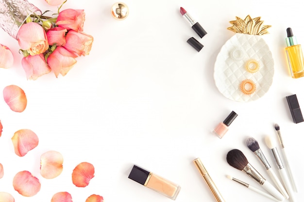 Table de bureau rose avec des fleurs, maquillage, pinceau et cosmétiques. Accessoires femme, concept de surface