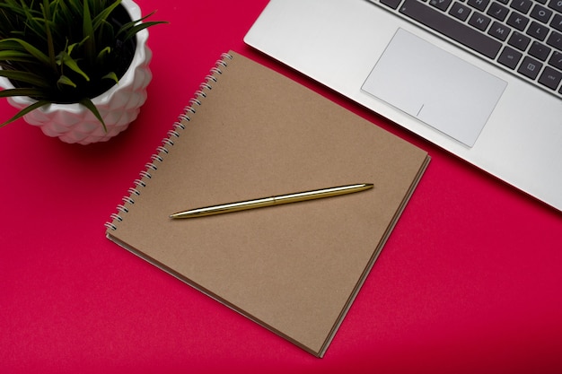 Table de bureau rouge avec stylo ordinateur portable et plante d'intérieur