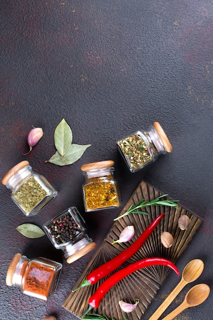 Photo table de cuisson avec des épices dans des bocaux en verre et des herbes. sur une surface sombre