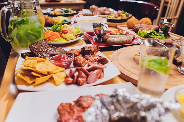 Table à dîner avec grill à la viande, pommes de terre nouvelles rôties, légumes, salades, sauces, collations et limonade, vue de dessus.