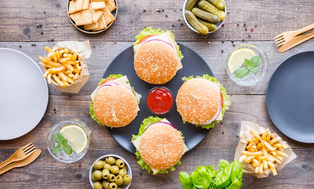 Table à dîner avec hamburger, frites, légumes, sauces, collations et limonade sur bois