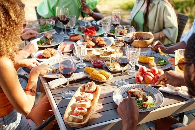 Table de dîner rustique à l'extérieur avec un délicieux festin fait maison et des personnes appréciant le repas d'été ensemble