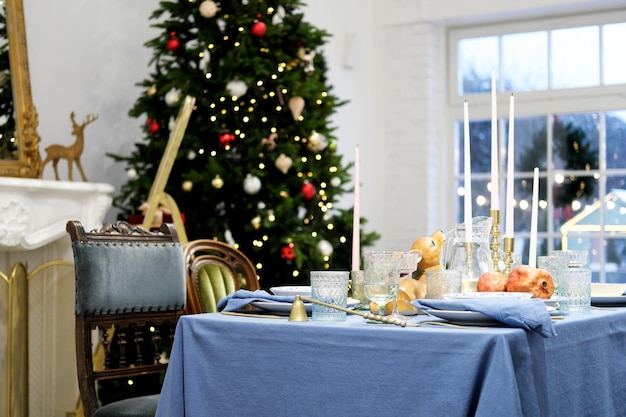 La table du dîner festif se dresse sur fond d'arbre de Noël Sur la table il y a une nappe bleue assiettes verres et décor