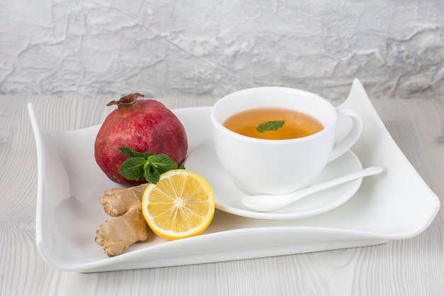 sur la table du thé dans une tasse, du gingembre, du citron, de la menthe et de la grenade sur un plateau. Espace libre pour le texte