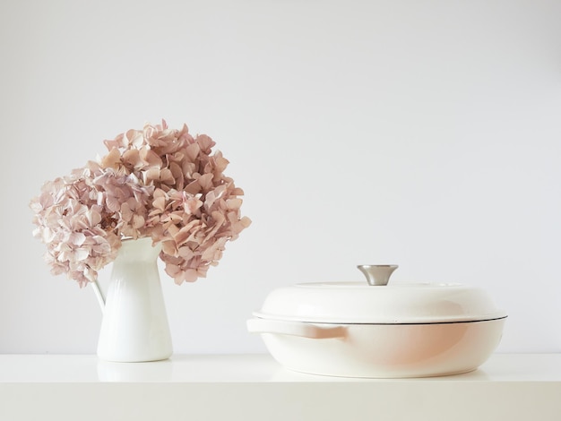 Table élégante et simple avec pot blanc et vase avec fleurs d'hortensia roses séchées Vue de face avec espace de copie sur fond de mur blanc cassé