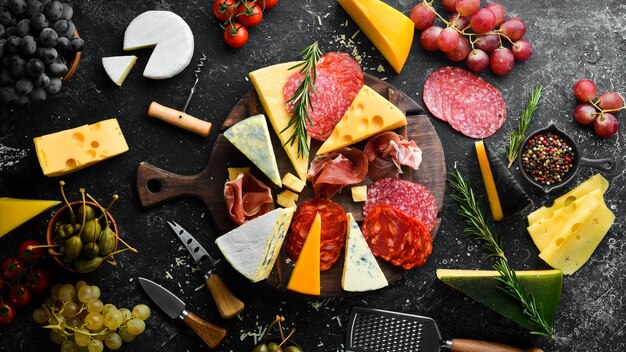 Table d'entrées avec des collations antipasti italiennes et du vin dans des verres Salami au vin de fromage et prosciutto sur fond de pierre noire Vue de dessus Espace libre pour votre texte